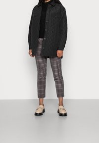 Black quilted jacket with snap buttons, textured fabric, paired with checkered cropped pants and cream loafers with decorative hardware.