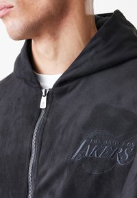 Crna zip-up hoodie od mekog materijala, sa vezanim logotipom "Los Angeles Lakers" i kengurudžerskom džepom.