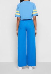 Sudadera azul recortada con franjas amarillas en las mangas, combinada con pantalones amplios azules. Ambas prendas están hechas de una tela suave.