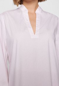 Blouse rose clair avec un motif à rayures verticales, col mandarin et un décolleté en forme de goutte. Confectionnée dans un tissu lisse et léger.