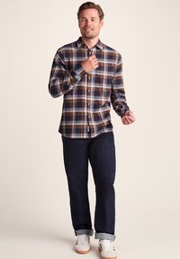 Button-up plaid shirt featuring navy, white, and orange colors; long sleeves; classic collar; paired with rolled dark jeans and white sneakers.