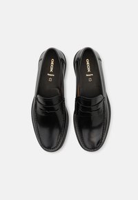 Scarpe slip-on in pelle nera con finitura lucida, caratterizzate da un dettaglio cucito lungo i bordi e un logo sottile sulla soletta.