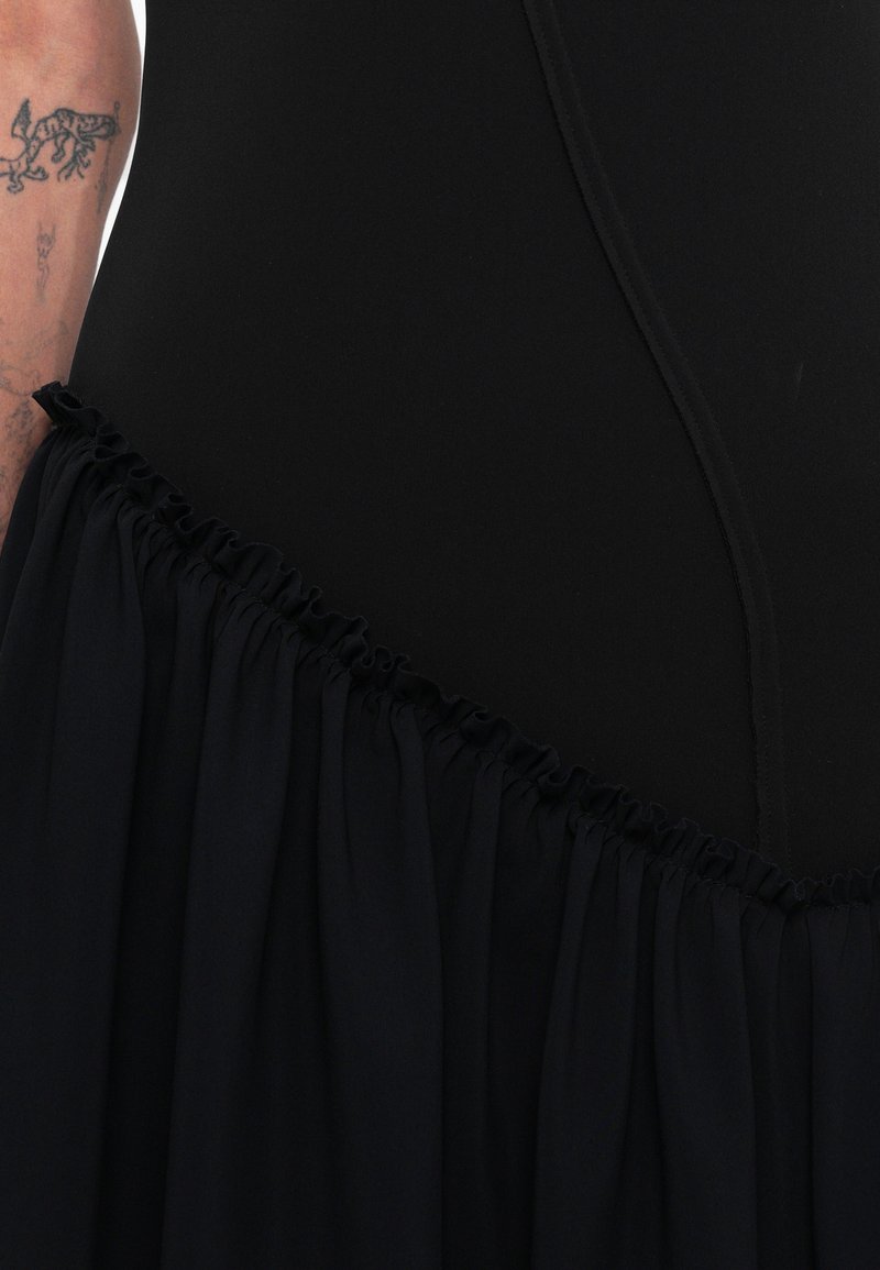 Black dress featuring a fitted top with a smooth texture and a flared, ruffled skirt in contrasting fabric. Seam details are visible.