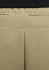 Beige sweatpants med en slät yta och elastiskt midjeband. Har en sydd sömdetalj som går vertikalt längs ryggen.