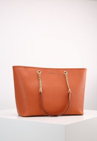 Grande borsa a spalla in pelle arancione con accenti in catena dorata e doppi manici, caratterizzata da una superficie liscia e un dettaglio del logo sulla parte anteriore.