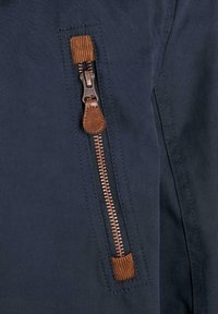 Navy fabric with a brown leather-accented zip pocket. Features a visible metal zipper and sturdy stitching. Smooth texture.