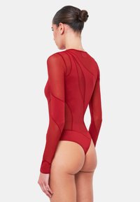 Röd långärmad bodysuit med en kombination av fasta och genomskinliga mesh-paneler, stilren design, figurnära silhuett och hög skärning bak.