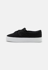 Schwarze Canvas Slipper mit einem geknoteten Design, ausgestattet mit einer weißen Gummisohle und einem gepunkteten Muster im Innenfutter.