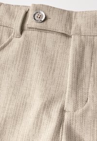 Beige strukturierte Hose mit einem Knopfverschluss mit einem glänzenden silbernen Rand, einem kunstvollen Webmuster und seitlichen Taschen.