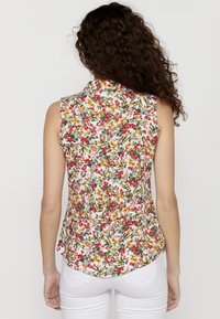 La blusa senza maniche a fiori presenta uno sfondo bianco con fiori colorati in rosso, giallo e verde. Design con colletto e orlo curvo.