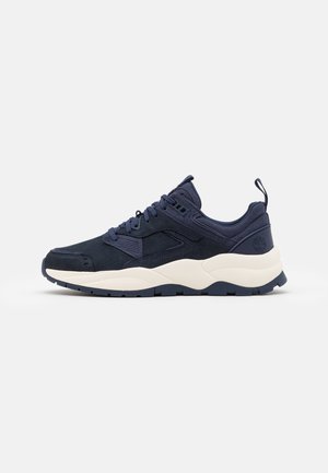 Mørkeblå atletiksneaker med tyk hvid sål, snørebånd og polstret krave, vist fra ydersiden mod hvid baggrund.