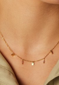 Gouden ketting met kleine geometrische hangers en gekleurde kralen, met een fijn ontwerp en een gladde, glanzende afwerking.