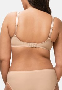 Béžová podprsenka s nastavitelnými ramínky a zapínáním na háček a očko. Hladký povrch s minimem švů. Viditelné doplňkové béžové spodní prádlo.