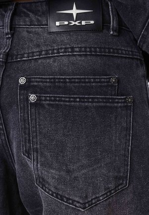 Dark denim jeans featuring two back pockets, silver hardware accents, and a black leather label with "PXP" logo at the waistband.