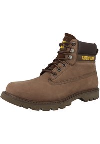 Botas de cuero marrón hasta el tobillo con un cuello acolchado, suela de goma con patrón estriado, ojales de metal y un logo visible en el lateral.