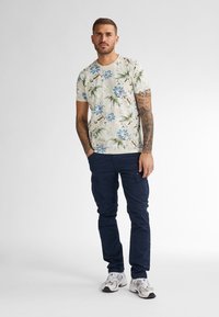 Floral shirt met korte mouwen met blauwe en groene patronen op een lichte achtergrond, gecombineerd met marineblauwe cargobroeken en witte sneakers.