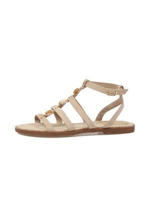 Sandalia plana beige con tira en el tobillo y piedras decorativas de tono dorado en varias tiras finas a lo largo del pie.