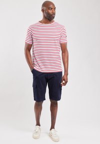 Camiseta a rayas rojas y blancas con escote redondo, combinada con pantalones cortos cargo azul marino. Estilo casual con mangas cortas y bolsillos laterales.