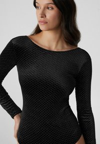 Body de manga larga negro hecho de tela suave con un patrón de diamantes y detalles plateados, con un escote amplio y diseño ajustado.