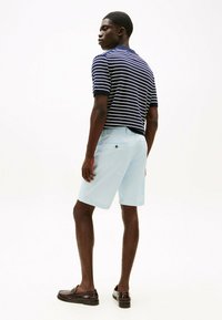 Polo a maniche corte a righe blu navy e bianche abbinato a pantaloni corti azzurri, con tasca sul retro e dettaglio di bottone marrone.