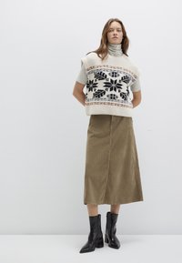Knitted cream sweater with black floral design, paired with a khaki midi skirt. Model wears black pointed ankle boots.