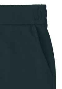 Gros plan d'un pantalon en tissu noir avec une taille élastique et une poche latérale visible sur le côté droit.