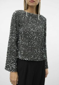 Top gris con lentejuelas y mangas largas, que presenta una superficie texturizada y un escote redondo. Combinado con pantalones negros, mostrado sobre un fondo claro.