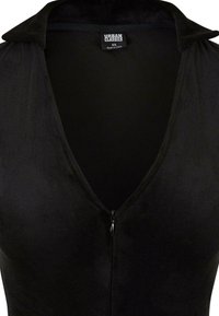 Body noir avec un décolleté en V profond, texture douce et design à col. Comprend une fermeture éclair sur le devant et une étiquette indiquant "Urban Classics."
