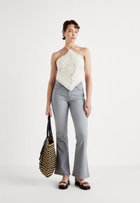 Top a halter all'uncinetto di colore bianco sporco, con un motivo a diamante. Abbinato a jeans svasati grigio chiaro e a una borsa a strisce nera e gialla.