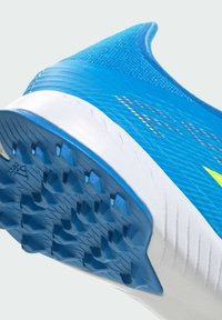 Gros plan sur la semelle d'une chaussure de sport bleue avec une semelle extérieure texturée antidérapante et une semelle intermédiaire blanche, mettant en avant les détails de traction et la tige en mesh léger.