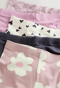 Cinco pares de leggings doblados apilados, con patrones florales, rosa sólido, corazón, azul marino y grandes flores blancas sobre fondo rosa.