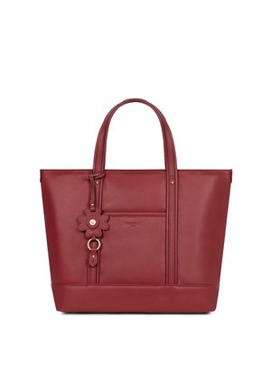 Sac fourre-tout en cuir rouge avec deux poignées, une poche avant et un charm décoratif en forme de fleur suspendu à une des poignées.
