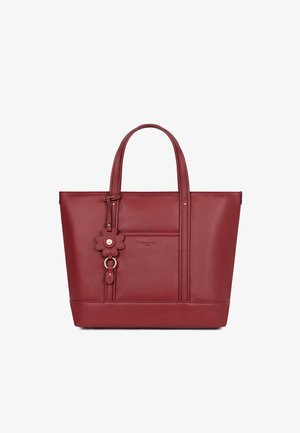 Sac fourre-tout en cuir rouge avec deux poignées, une poche avant et un charm décoratif en forme de fleur suspendu à une des poignées.