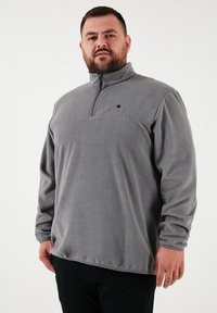 Grå fleece pullover med en kvart-zip krave. Har lange ærmer og et lille sort logo på brystet. Blød tekstur og afslappet pasform.