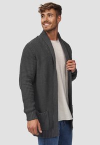 Cardigan lavorato a maglia di colore grigio scuro, con maniche lunghe, colletto a scialle e tasche laterali. La trama è a coste e presenta una vestibilità comoda.