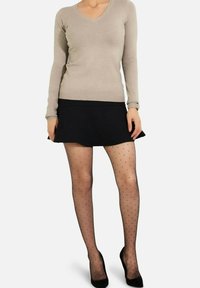 Haut beige à manches longues, jupe noire évasée et collants noirs transparents avec des pois. Des talons hauts noirs complètent la tenue.