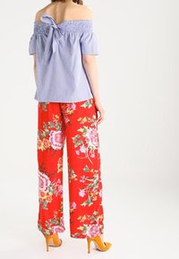 Blue and white striped off-the-shoulder top with a back bow, paired with high-waisted red floral wide-leg pants and yellow heels.