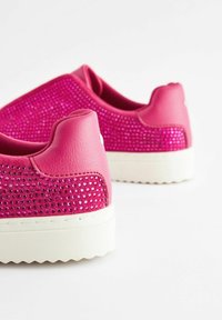 Zapatillas rosas con una superficie texturizada, adornadas con brillantes strass. Cuentan con una suela de goma blanca y un diseño de parte trasera redondeada.