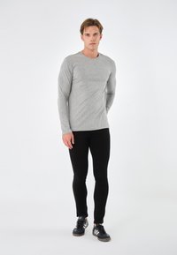 Gray long-sleeve shirt with a fitted design, paired with black skinny jeans and black athletic shoes featuring light gray accents.