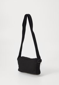Borsa a spalla in tessuto nero con una forma rettangolare elegante, cintura regolabile e chiusura con zip, caratterizzata da una superficie testurizzata.
