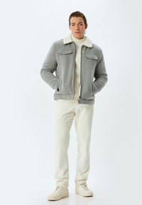 Grå lynlåsjakke med en cremefarvet faux fur krave, to brystlommer, parret med en cremefarvet ribbet sweater og bukser samt beige sneakers.