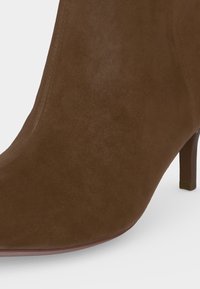 Bottine en daim marron avec un bout pointu et un talon fin de hauteur moyenne sur fond blanc.