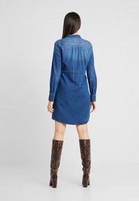Abito camicia in denim con maniche lunghe, vita aderente e orlo curvo. Gradiente di colore denim dal scuro al chiaro, abbinato a stivali alti fino al ginocchio con stampa serpente.