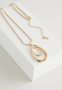 Gold-tone necklace with a curved pendant featuring a smaller oval surrounded by small clear gemstones. Adjustable chain and clasp included.