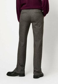 Gray patterned trousers with a tailored fit, featuring back pockets and a smooth texture, paired with black stylized shoes.