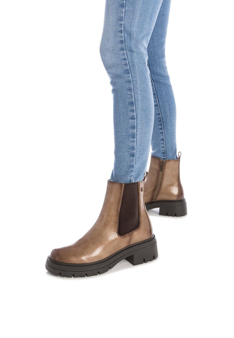 Botines marrones con acabado brillante, paneles laterales elásticos y un patrón texturizado. Suela de goma negra gruesa y detalle de tab de tirón trasero.