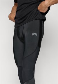 Svarta träningsleggings med en slät textur, åtsittande design och subtil logotyp på låret. Inkluderar kontrasterande sömmar.