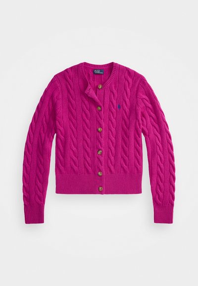 Roza pletena jopica z vzorcem kabelov, okroglo izrezano ovratnico, spredaj zapenjanje na gumbe z rjavimi gumbi ter rebrastimi manšetami in robom.