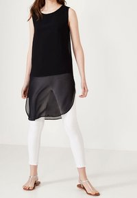 Black sleeveless tunic with a layered, sheer bottom, paired with white fitted leggings and silver flat sandals. Smooth texture, minimal design.