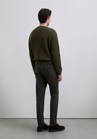 Olivengrøn ribstrikket sweater, grå bukser og mørkebrune sko. Modellen ses bagfra mod en lysegrå baggrund.